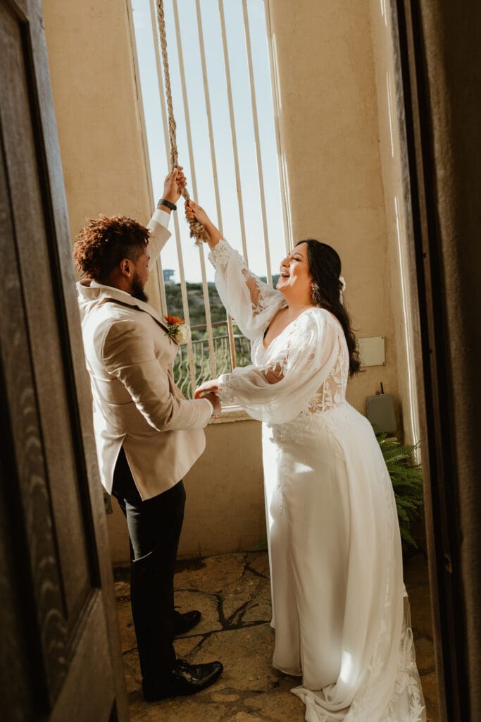 A couple ringing the wedding bells during an intimate wedding ceremony at Chapel Dulcinea in Austin, Texas, on a sunny day, with clear skies and natural surroundings.