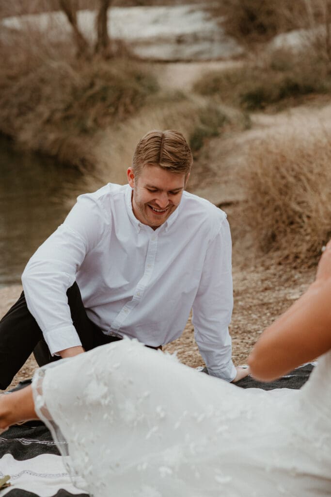 A couple sitting on a picnic blanket, smiling and enjoying a cloudy afternoon at McKinney Falls State Park.