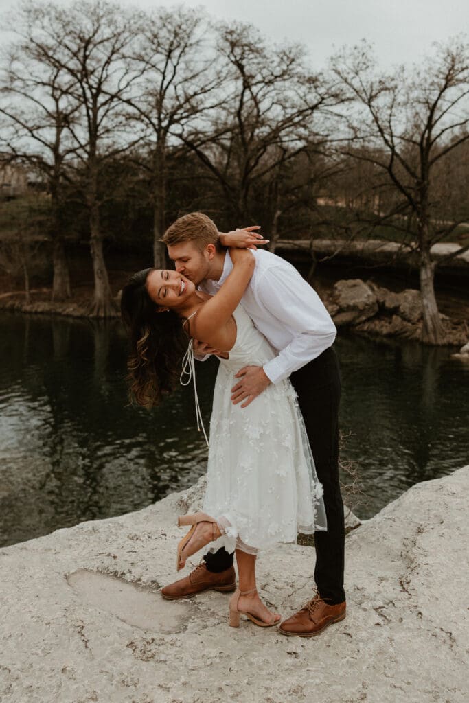 A couple looking cozy on a rocky cliff, with a scenic view of the landscape in the background at McKinney Falls State Park in Austin, Texas.