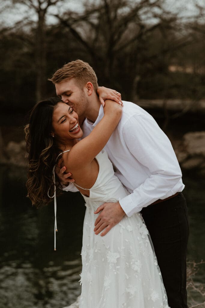 A couple hugging on a rocky cliff, with a scenic view of the landscape in the background at McKinney Falls State Park in Austin, Texas.