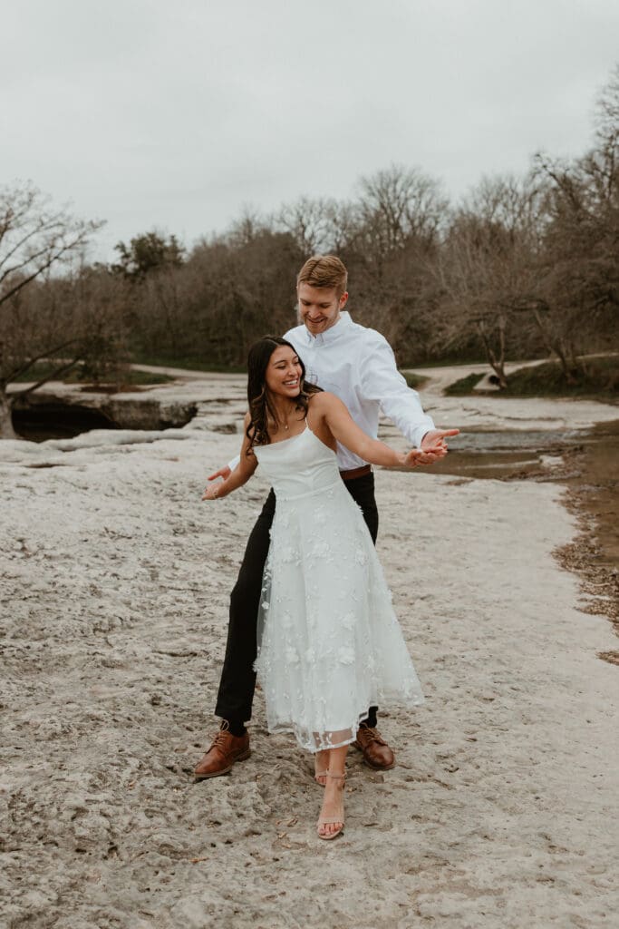 A couple embracing each other on a rocky cliff, with a scenic view of the landscape in the background at McKinney Falls State Park in Austin, Texas.