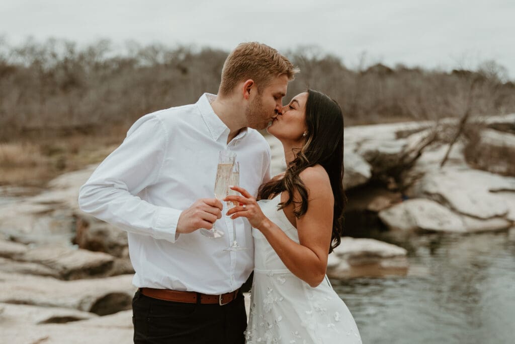 An engaged couple celebrating with a toast overlooking the cliffs at McKinney Falls State Park.