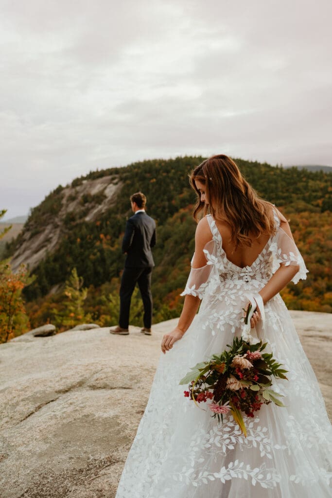 A couple preparing for their first look on a cloudy autumn evening in the mountains of New Hampshire, surrounded by colorful fall foliage.