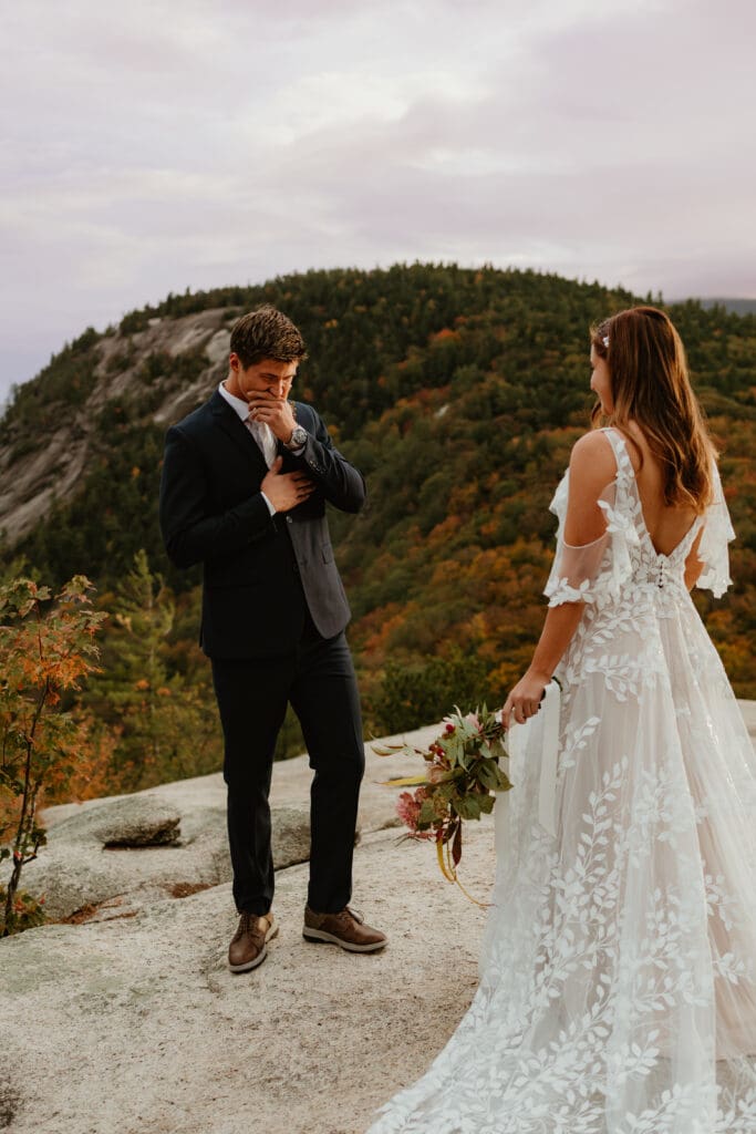 A couple embracing their first look on a cloudy autumn evening in the mountains of New Hampshire, surrounded by colorful fall foliage.