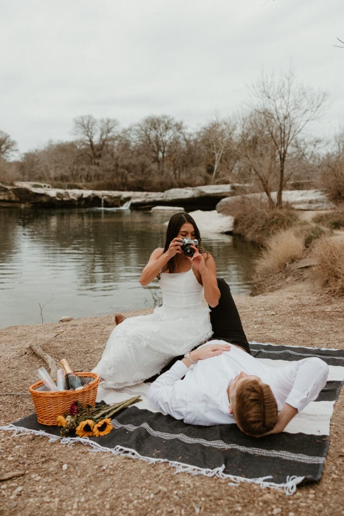 A playful engagement photo session of a couple sitting on a picnic blanket at McKinney Falls State Park in Austin, Texas.