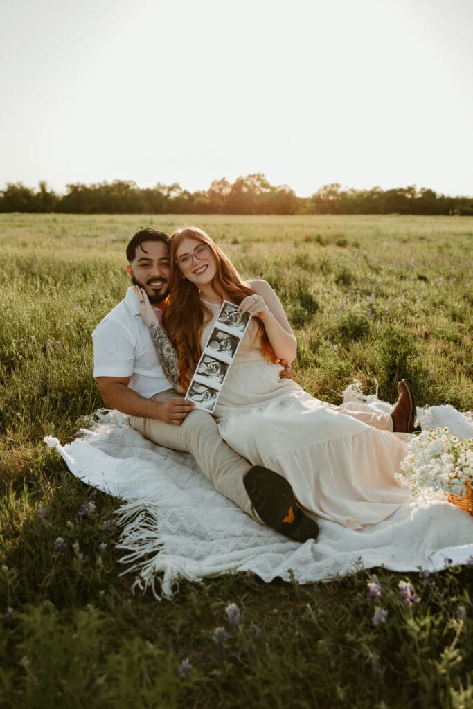 Expecting parents cozied together holding sonogram during a golden hour photo session in Cedar Park, Texas.