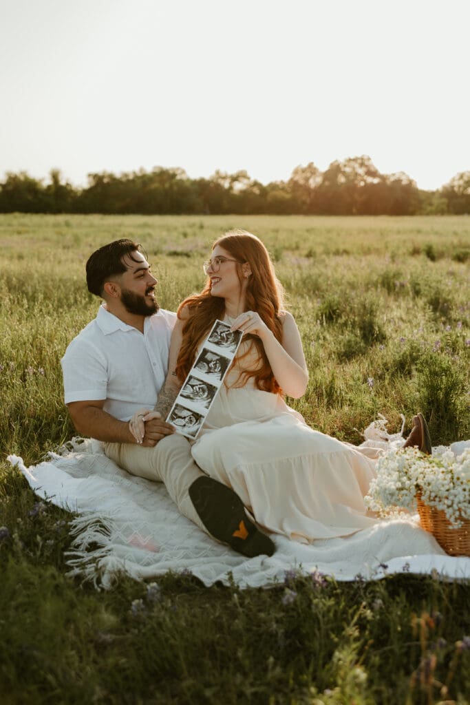 Expecting parents looking at each other while holding sonogram during a golden hour photo session in Cedar Park, Texas.