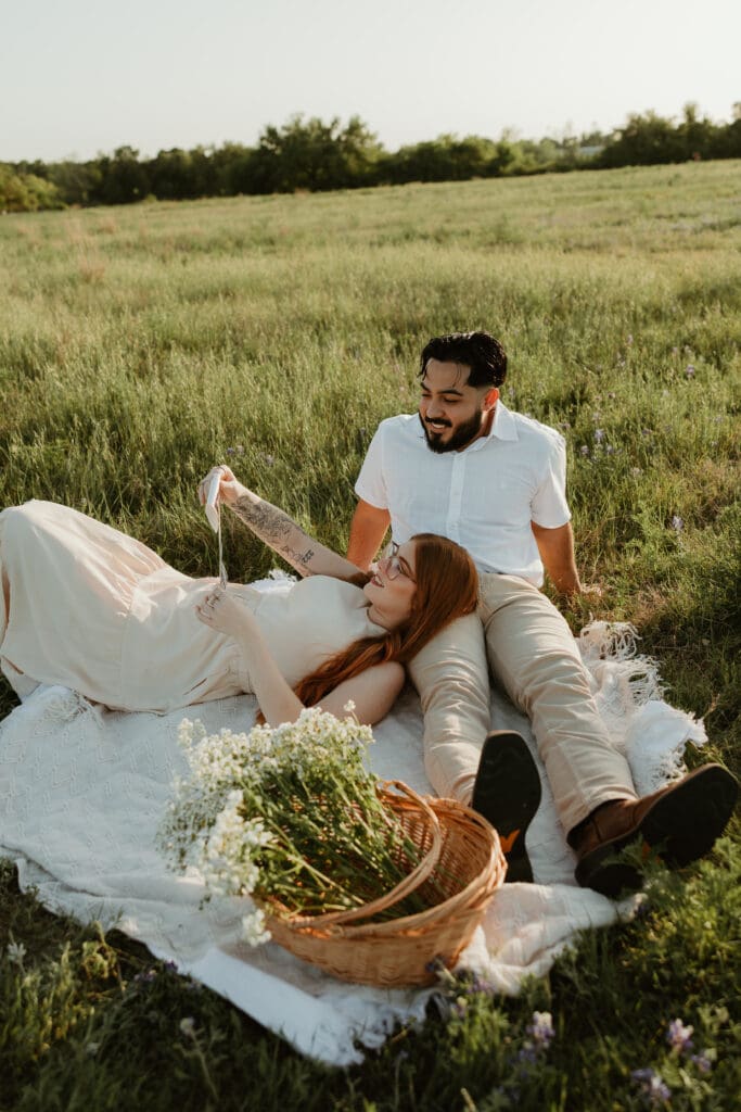 Couple sitting together on a picnic blanket, showcasing baby sonogram with dreamy sunset lighting.