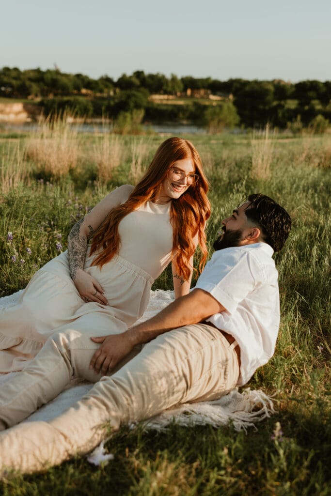 Couple sitting together on a picnic blanket, holding baby bump during photo session at Brushy Creek Lake Park.
