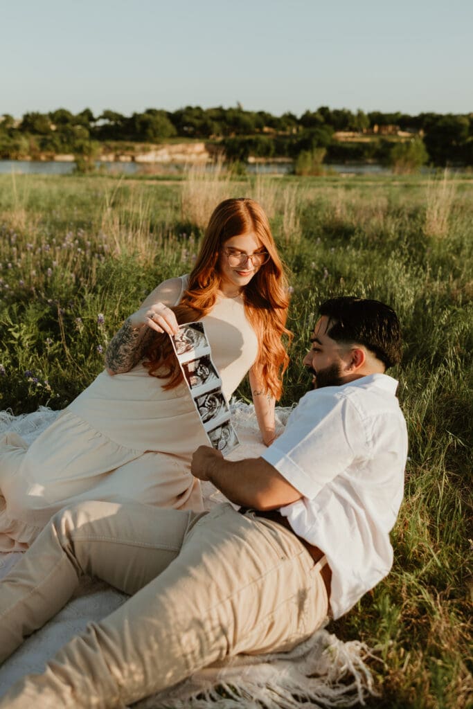 Couple sitting together on a picnic blanket, holding sonogram during photo session in Cedar Park, Texas.
