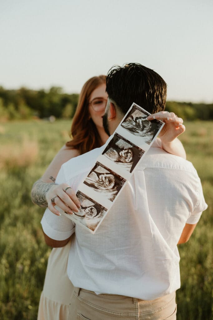 Pregnant couple standing in a field of wildflowers with an ultrasound image.