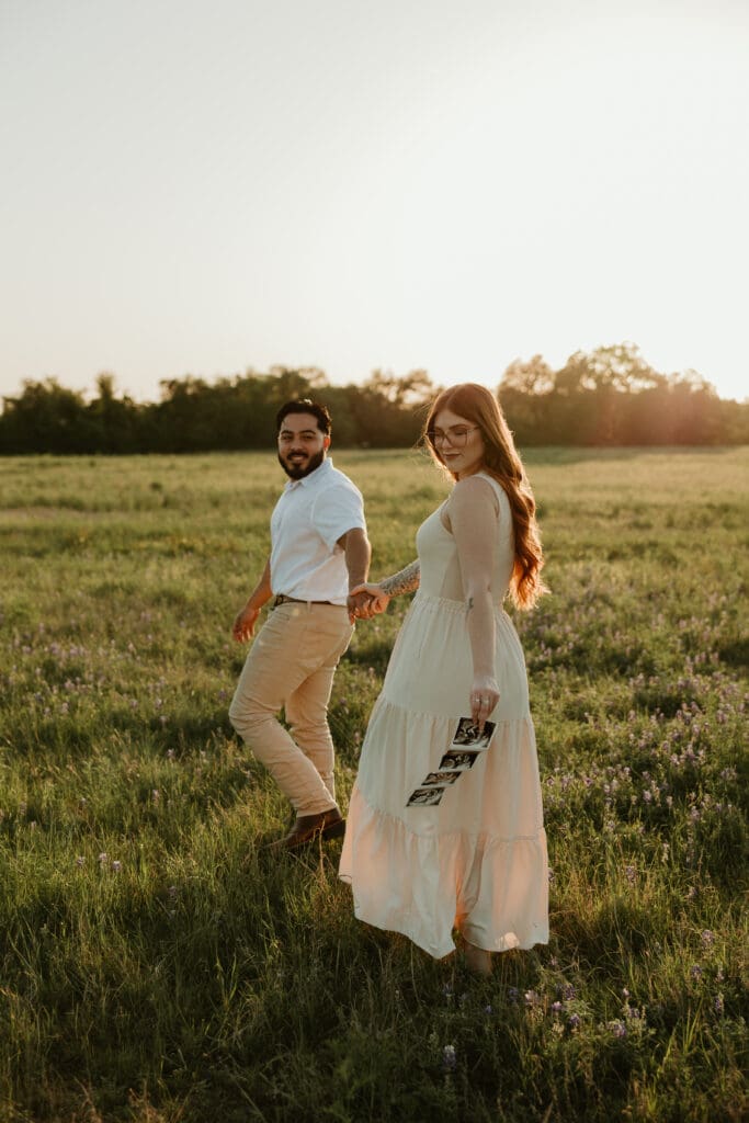 Expecting couple taking a stroll through a wildflower field while holding their sonogram. 