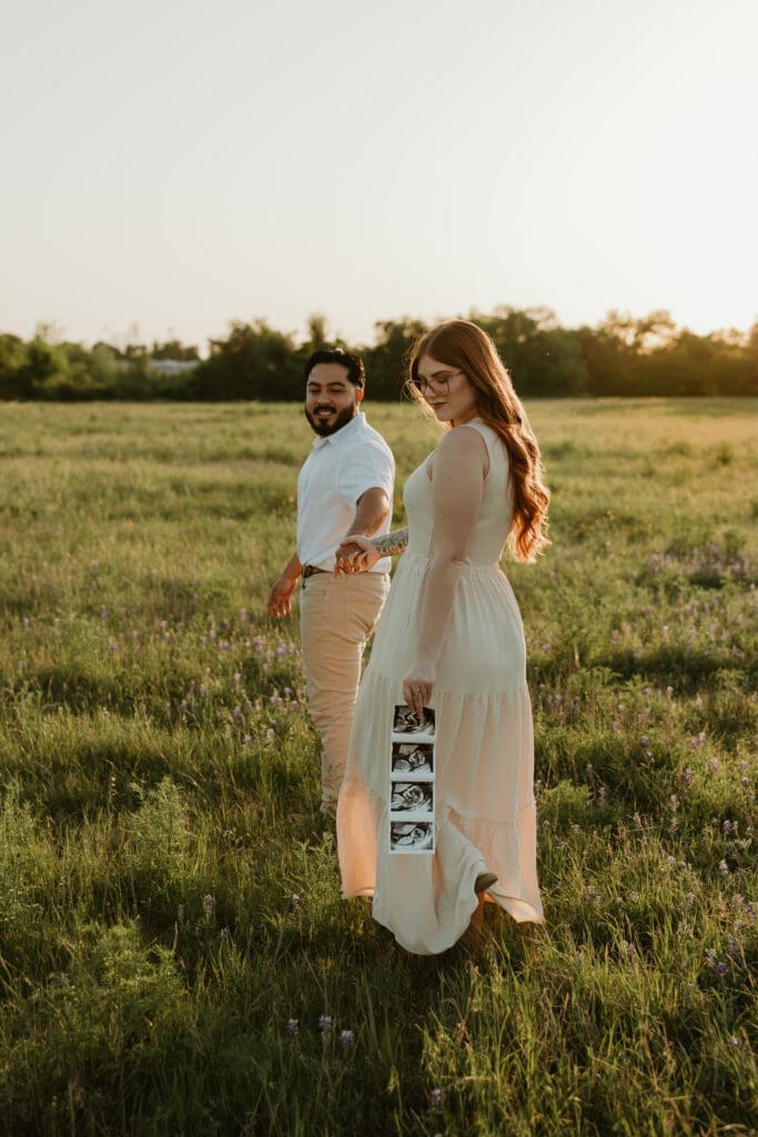 Expecting couple walking hand-in-hand at Brushy Creek Lake Park, with a sonogram in hand. 

