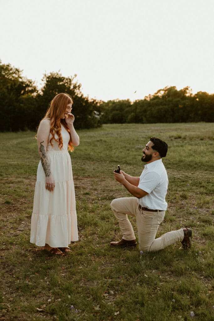 Woman covering her mouth in surprise as her partner proposes during their photo shoot.