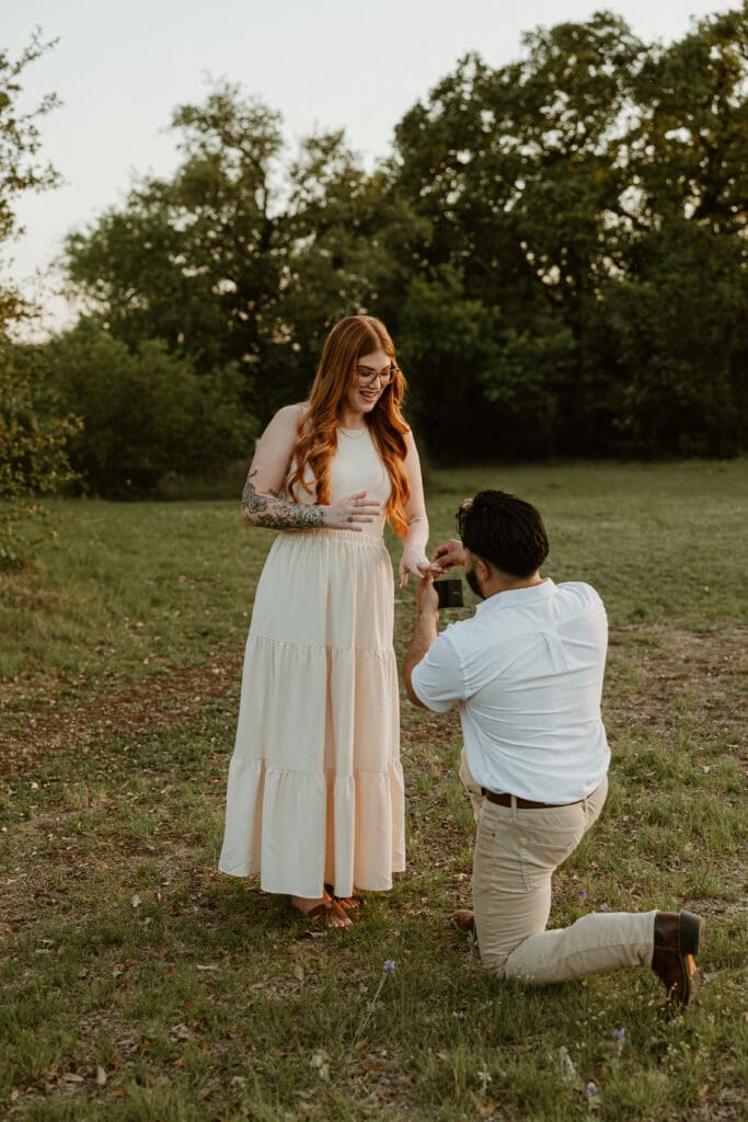 Proposal moment captured candidly with a soft background of trees and sunset light.