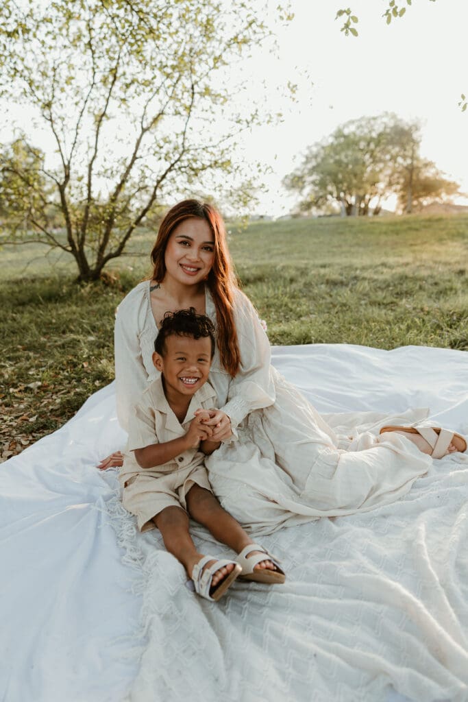 A candid moment of a mom and her son laughing together, surrounded by warm tones of sunset and greenery.