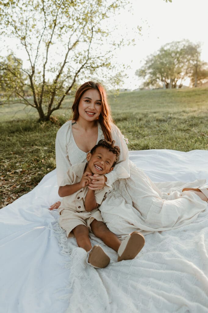 A candid moment of a mom and her son laughing together, surrounded by warm tones of sunset and greenery in a North Austin park.