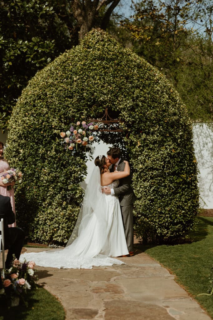Bride and Groom embracing their first kiss at their outdoor garden ceremony at the Hummingbird House