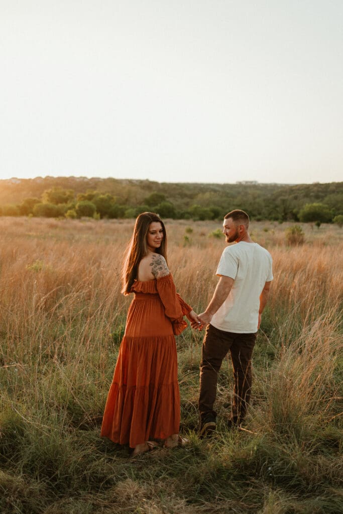 Expecting parents hold hands in open field during golden hour at Common Fords Ranch in Austin. 