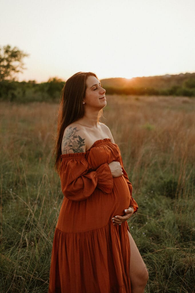 Expecting mom holds baby bump in open field during golden hour at Common Fords Ranch in Austin. 