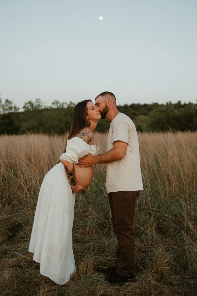 Expecting parents exchange a kiss in open field during blue hour at Common Fords Ranch in Austin. 