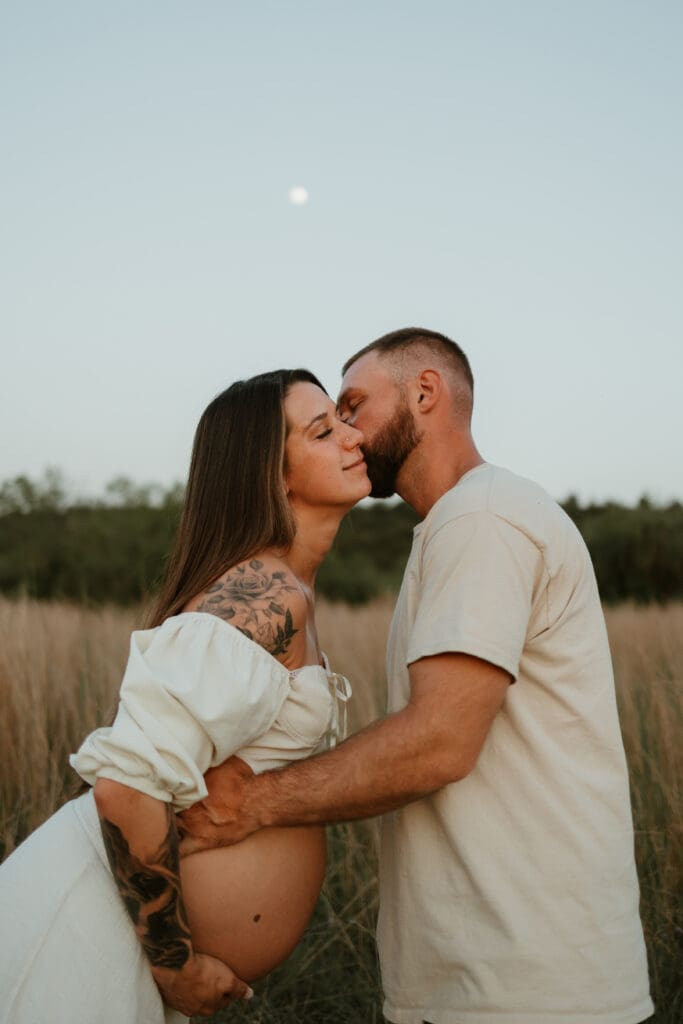 Expecting parents exchange a kiss in open field during blue hour at Common Fords Ranch in Austin. 