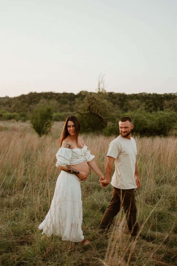 Expecting parents hold hands in open field during golden hour at Common Fords Ranch in Austin. 