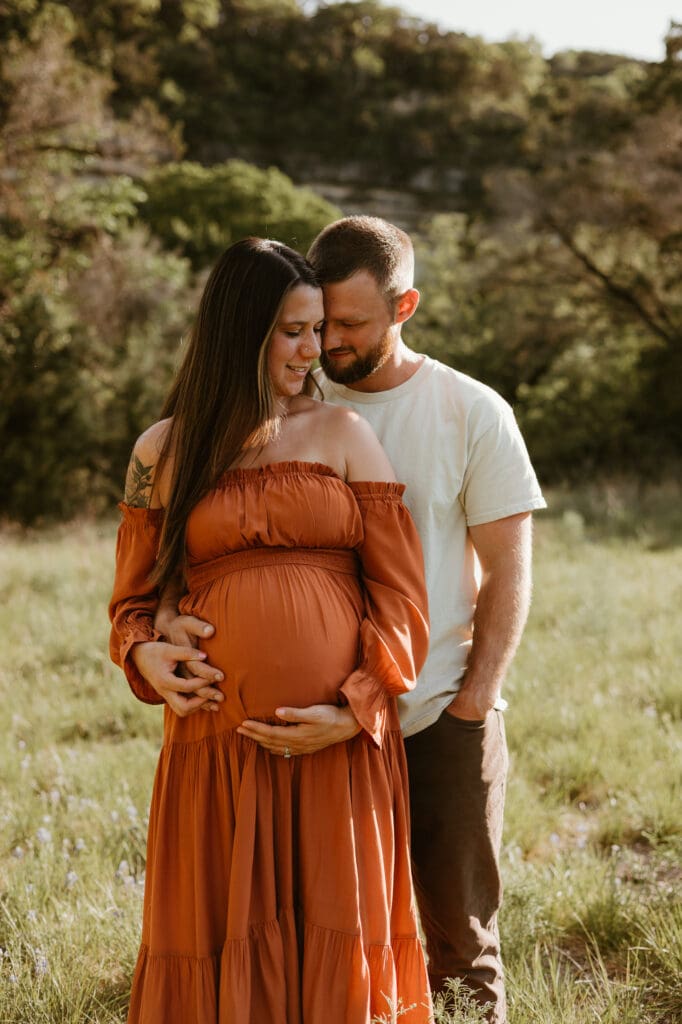 Expecting parents cuddle together during golden hour photoshoot in Austin. 