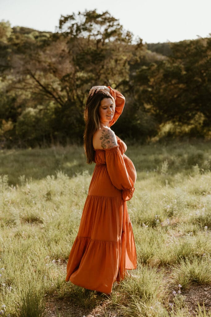 Mama to be holding baby bump during golden hour in open field in Austin. 