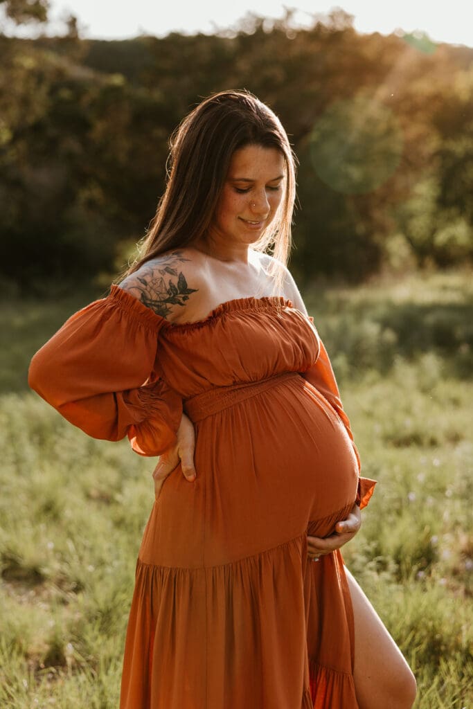 Mama to be holding baby bump during golden hour in open field in Austin. 