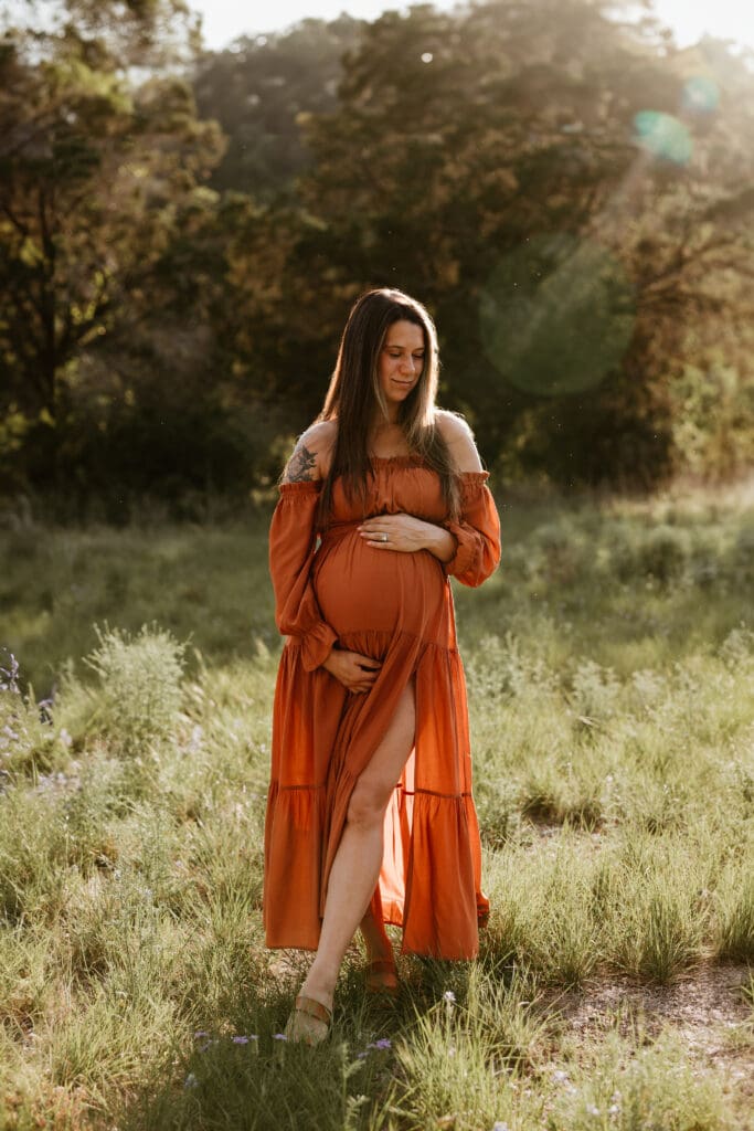 Mama to be holding baby bump during golden hour in open field in Austin. 