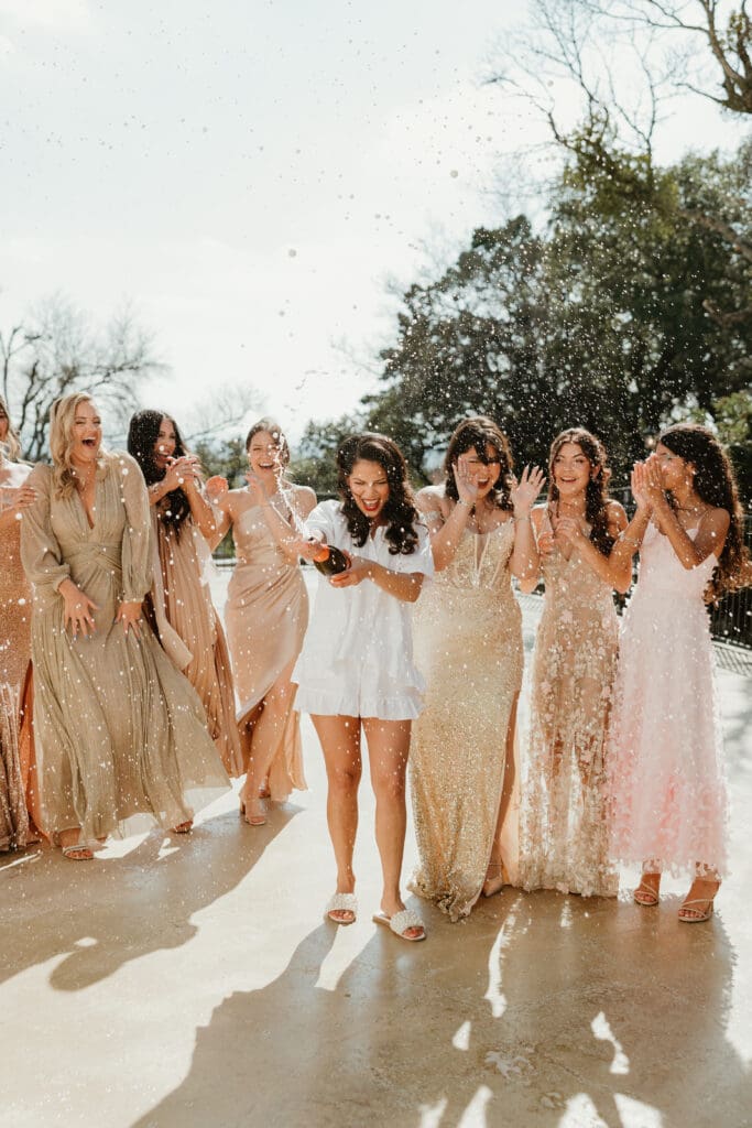 Bride and bridesmaids pop champagne on wedding day at Villa Antonia in Austin, Texas.