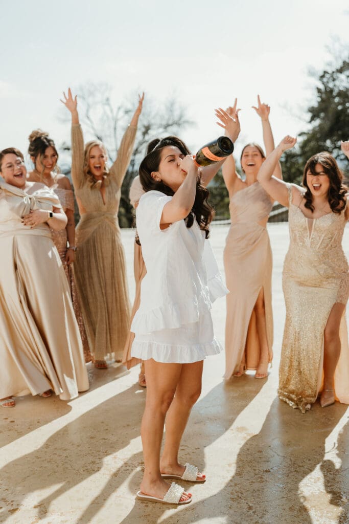 Bride and bridesmaids pop champagne on wedding day at Villa Antonia in Austin, Texas.
