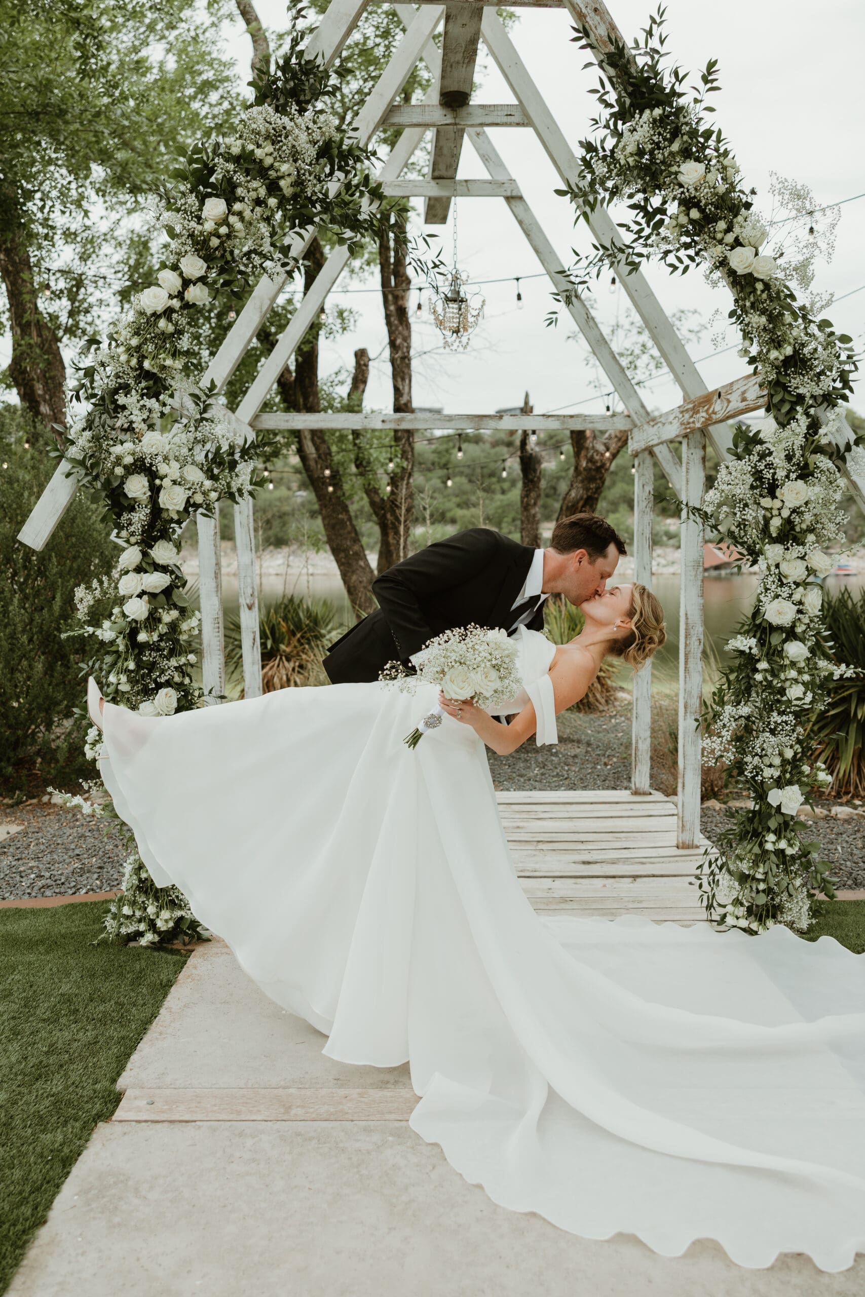 Bride and groom exchange kiss surrounded by lush florals at outdoor ceremony space at Blissful Hill wedding venue in Texas Hill Country.